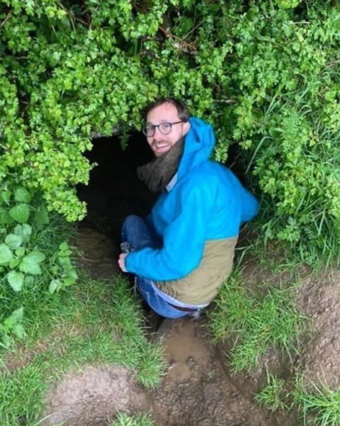 field image of Derek crouched at a mouth of a cave in Ireland